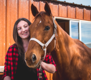 Woman smiling with a brown horse outside.