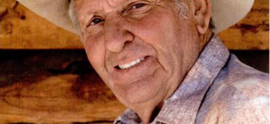 Smiling elderly man wearing a cowboy hat and plaid shirt.