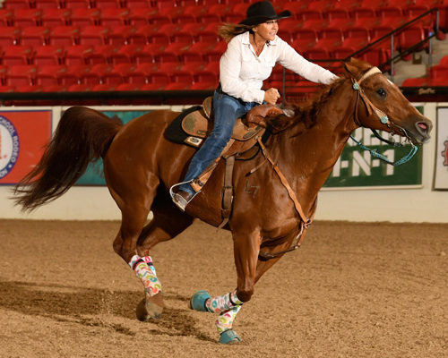 A rider in a cowboy hat guides a horse inside an arena.