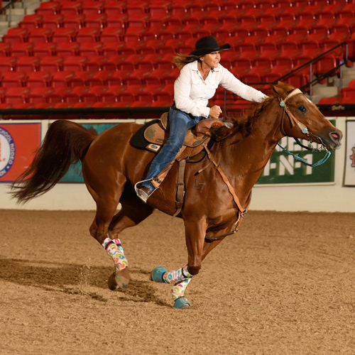 A rider in a cowboy hat guides a horse inside an arena.